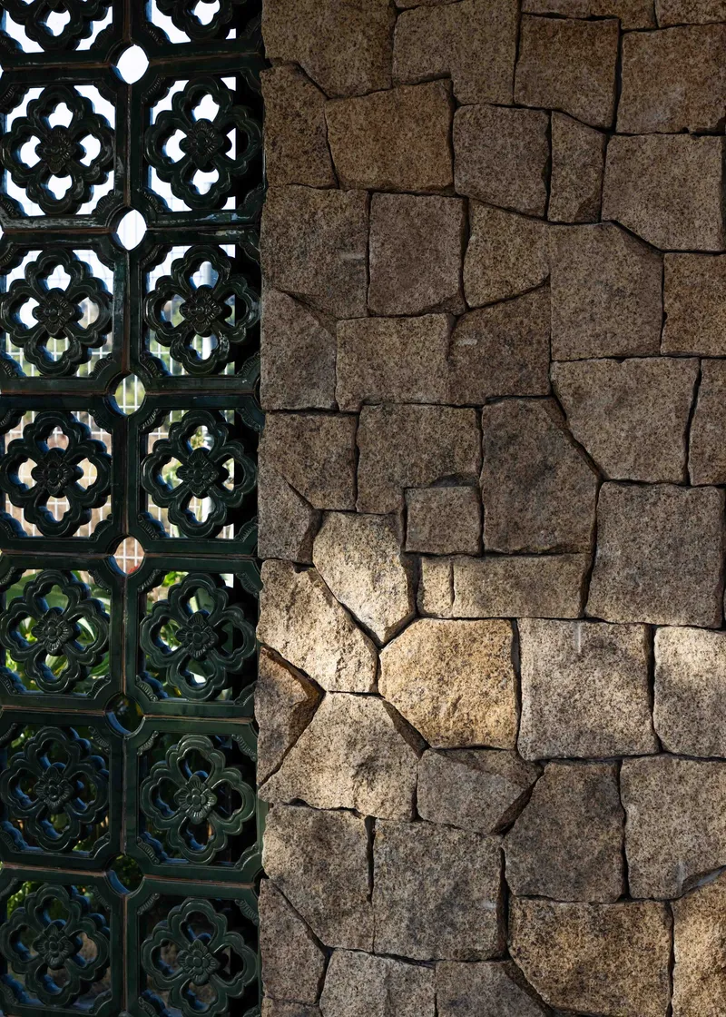Detail of patterned concrete screen beside rough-cut stone wall in dappled sunlight