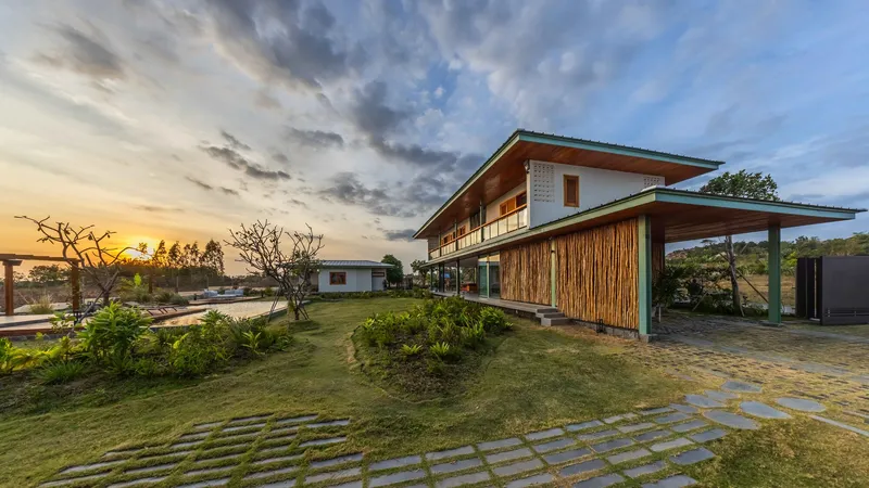 Front elevation showing bamboo-clad volume and open carport at sunset with dramatic clouds overhead