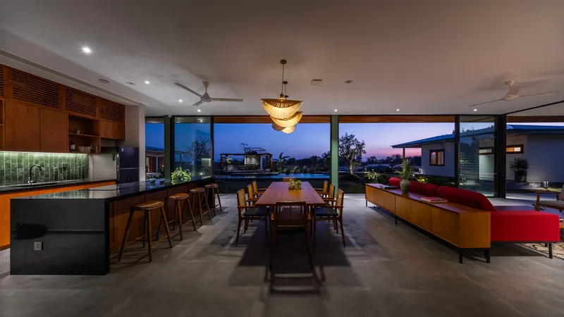 Open-plan kitchen, dining and living space with full-height glazing overlooking garden at dusk