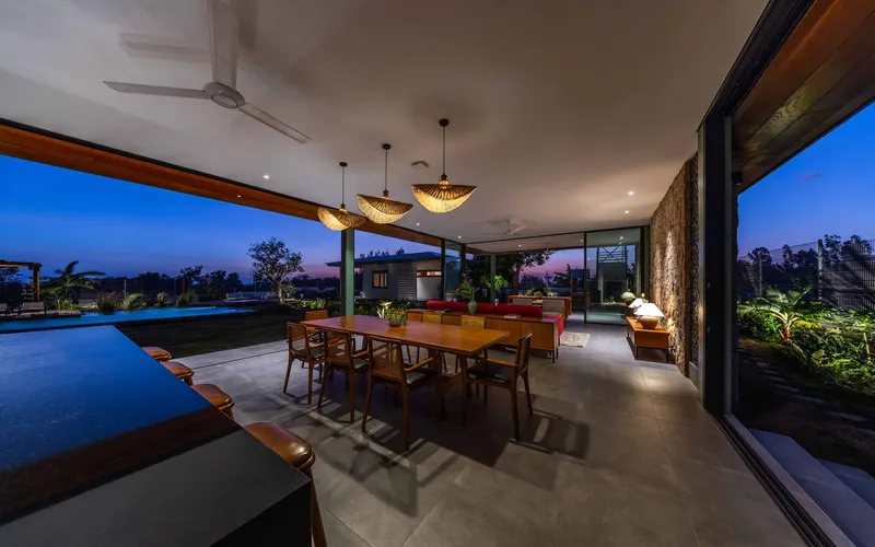 Covered terrace with dining table, pendant lights and adjacent pool at twilight
