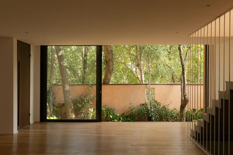 Interior room with timber floor and full-height glazing overlooking planted courtyard with vertical metal screens