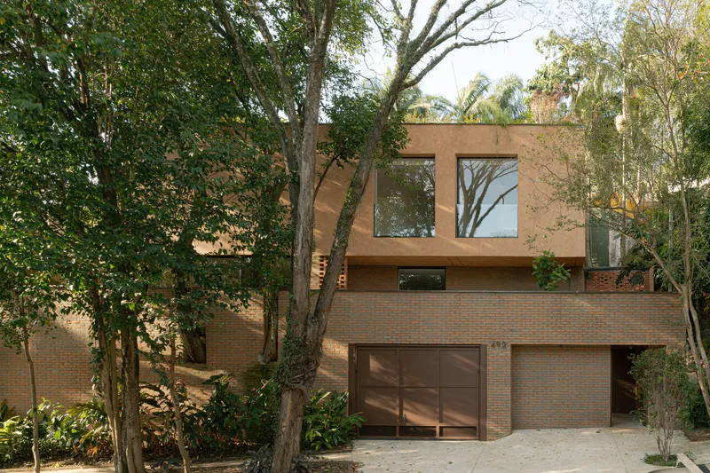 Street facade with brick base and timber-clad upper volume framed by mature trees