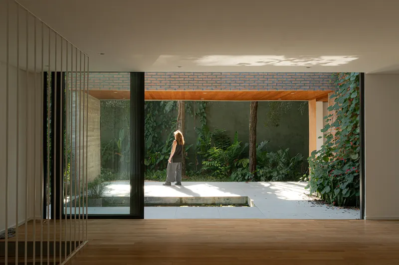 Interior view through sliding glass doors to a courtyard with a figure walking through dappled sunlight