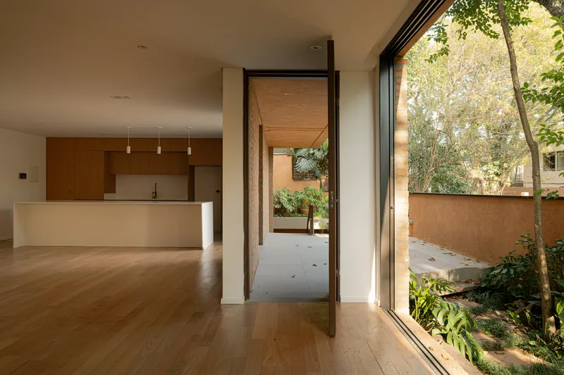 Open kitchen and living space with pivoting timber door leading to a planted courtyard