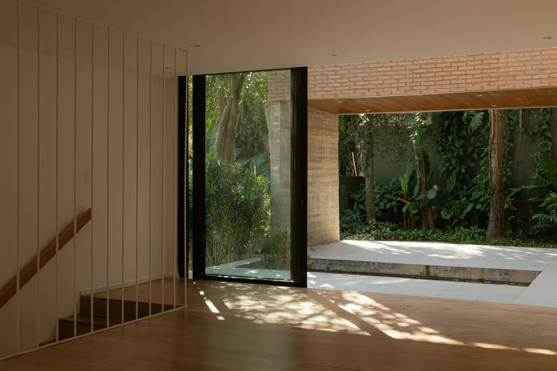Timber staircase alongside full-height glazing opening to a sunlit patio with exposed brick ceiling