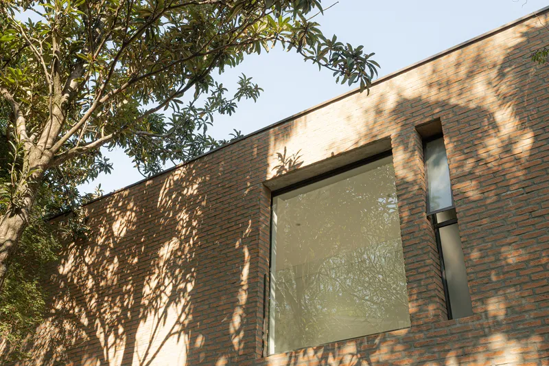 Brick facade with recessed window openings under dappled tree shadows in afternoon light