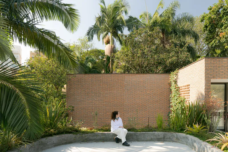Concrete bench in courtyard surrounded by brick wall and tropical palms with seated figure