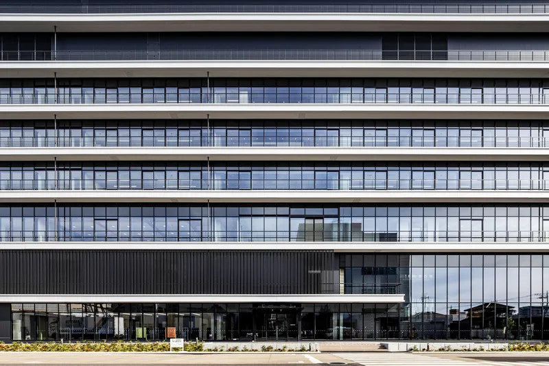 Facade showing horizontal bands of glazing with slender vertical mullions above a planted ground level