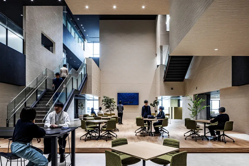 Double-height interior atrium with timber-clad walls and people seated at collaborative work tables