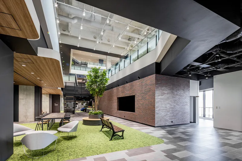Interior atrium showing red brick volume, artificial turf with seating, and exposed structural beams overhead