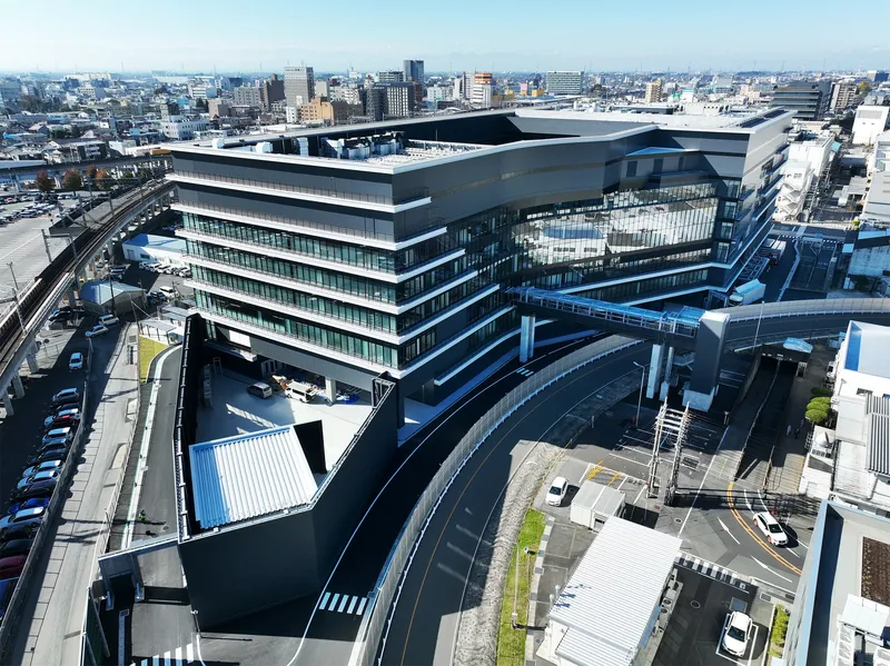 Aerial view of the stacked horizontal volumes with ribbon windows and an elevated steel bridge spanning the access road