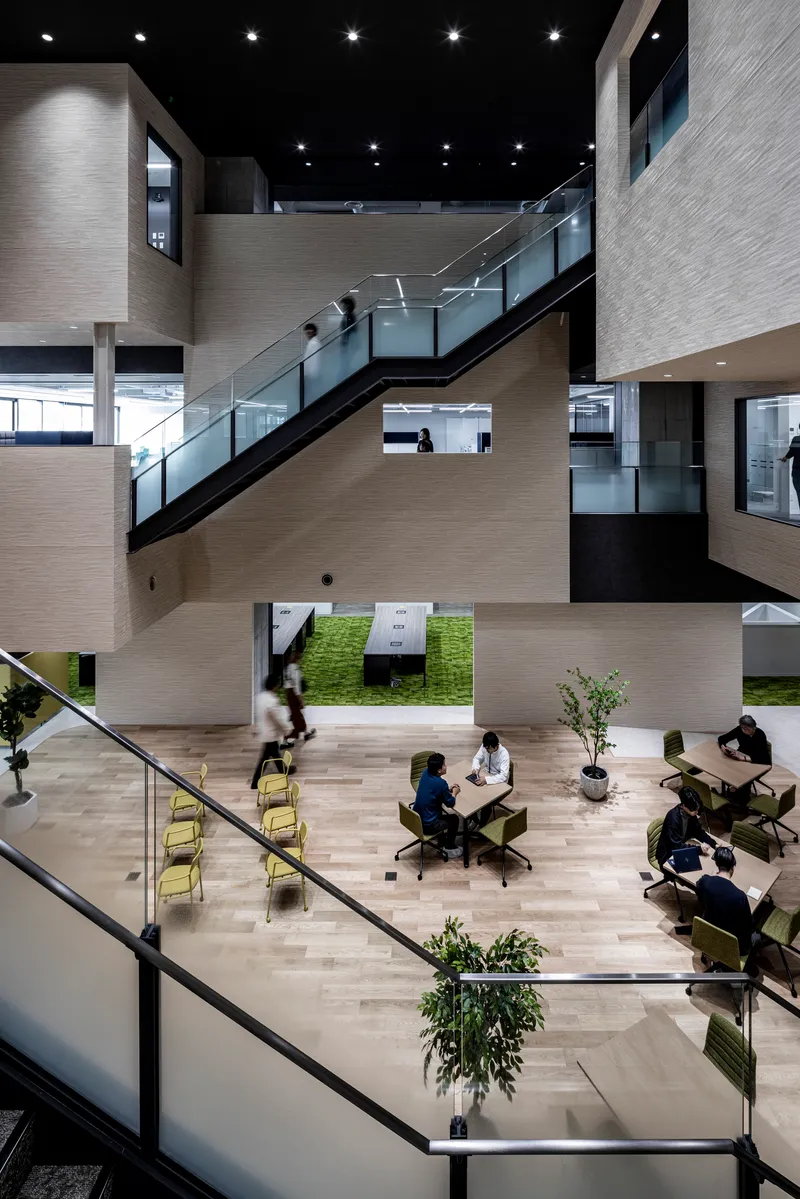 Atrium interior with metal-and-glass staircases linking floors, people seated at tables and a grass-covered courtyard below