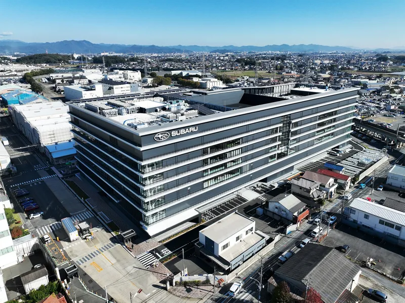 Elevated view of the horizontal-banded office building set among low-rise industrial structures and distant mountains
