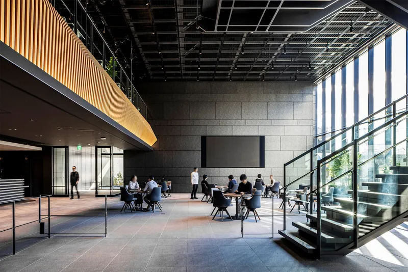 Double-height lobby space with large-format stone wall, glass-enclosed stair, and people at café tables