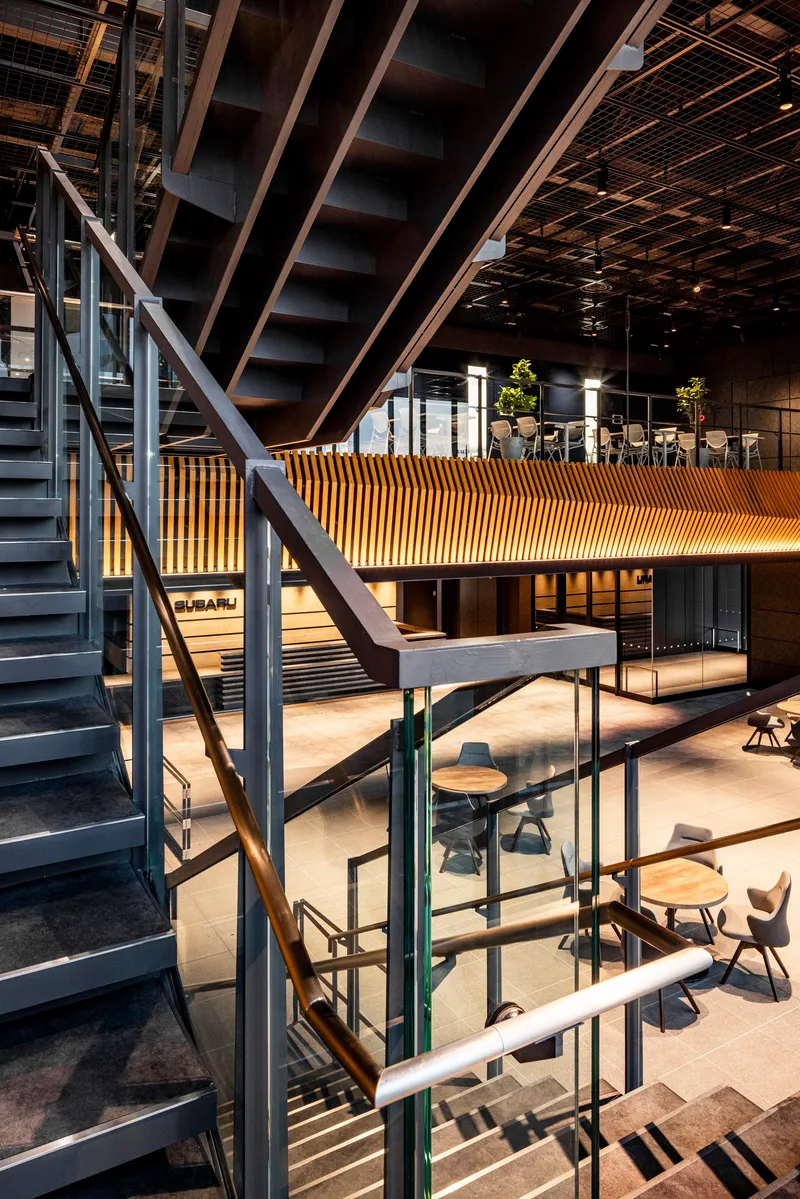 Vertical view of interconnected steel stairs, glass railings, and timber slatted bridge spanning between levels