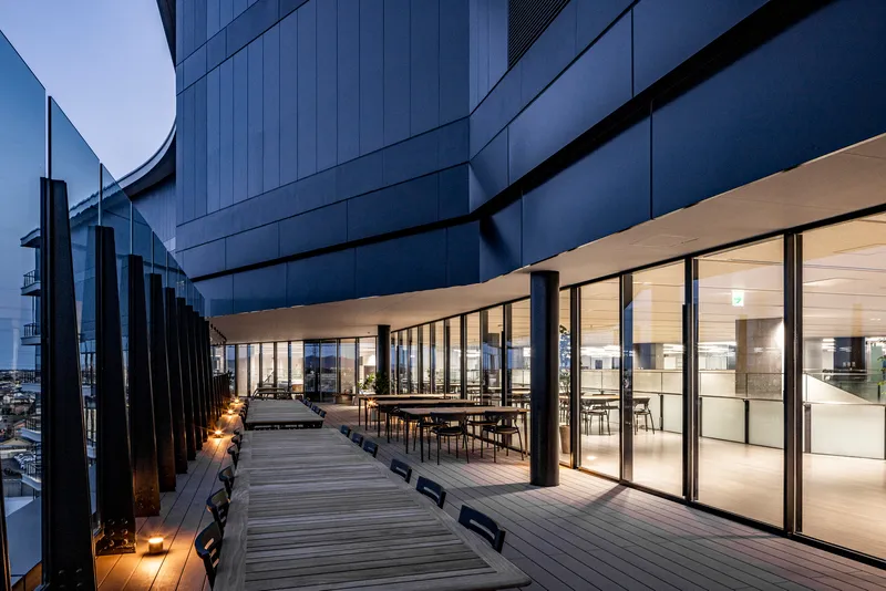 Timber deck terrace with glass-walled dining space and vertical metal fins at dusk