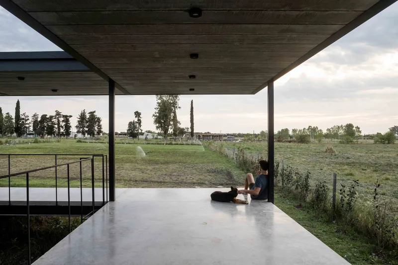 Covered terrace with timber ceiling where two figures sit on polished concrete floor overlooking fields