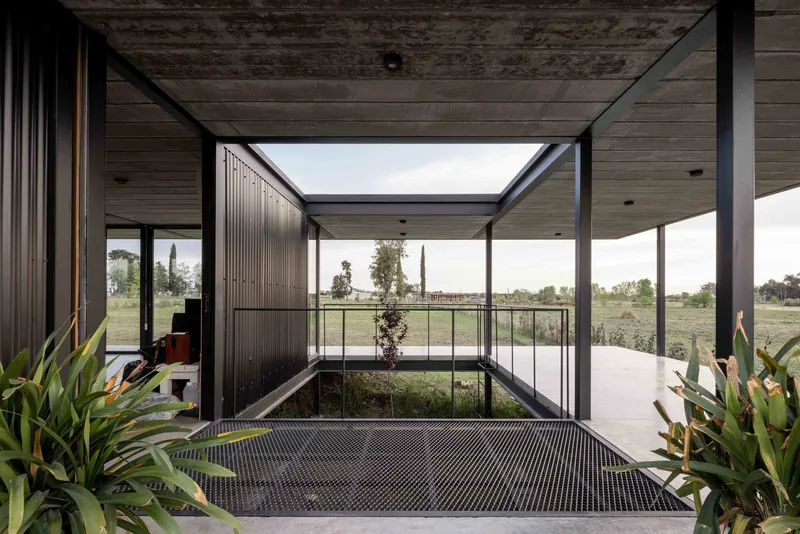 Covered entry passage framing a planted courtyard with metal grating and distant fields beyond