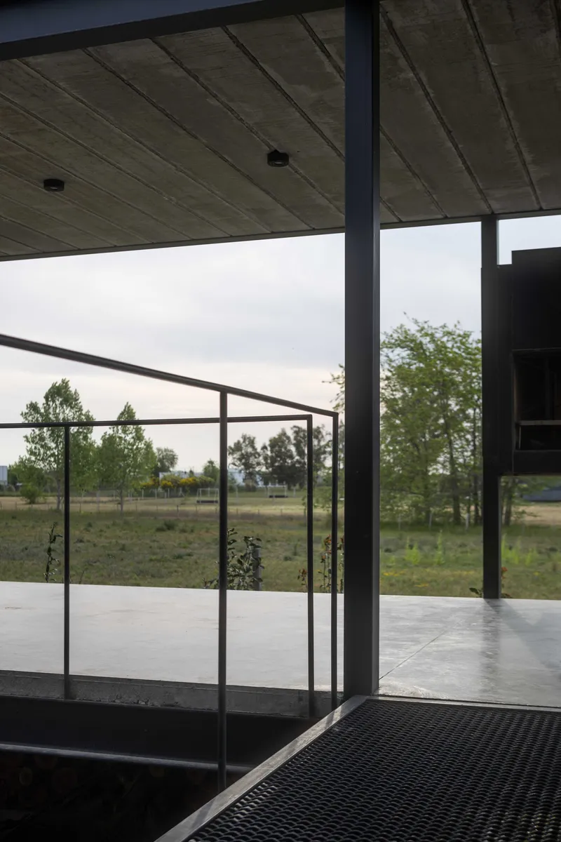View through steel-framed glass door opening onto covered terrace under overcast sky