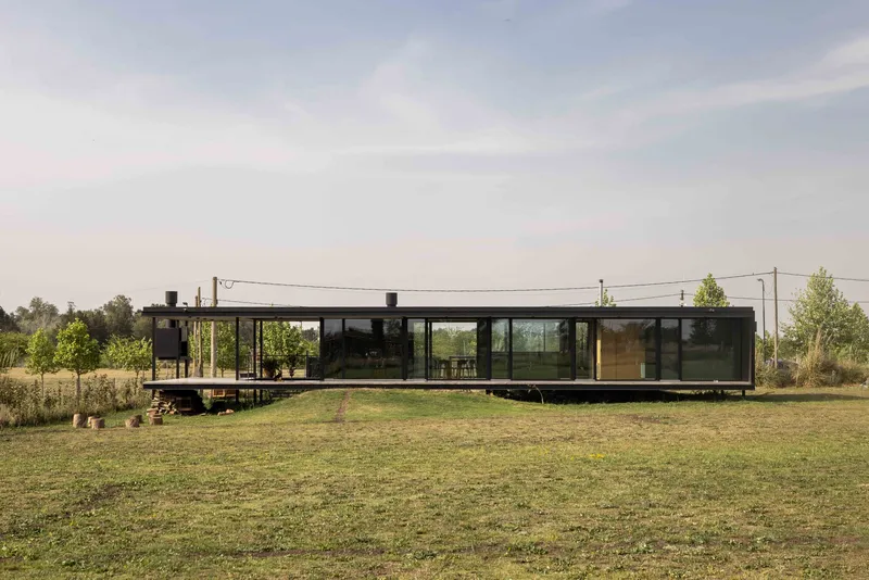 Long facade of dark-framed glass walls raised on a platform above the surrounding grassy field
