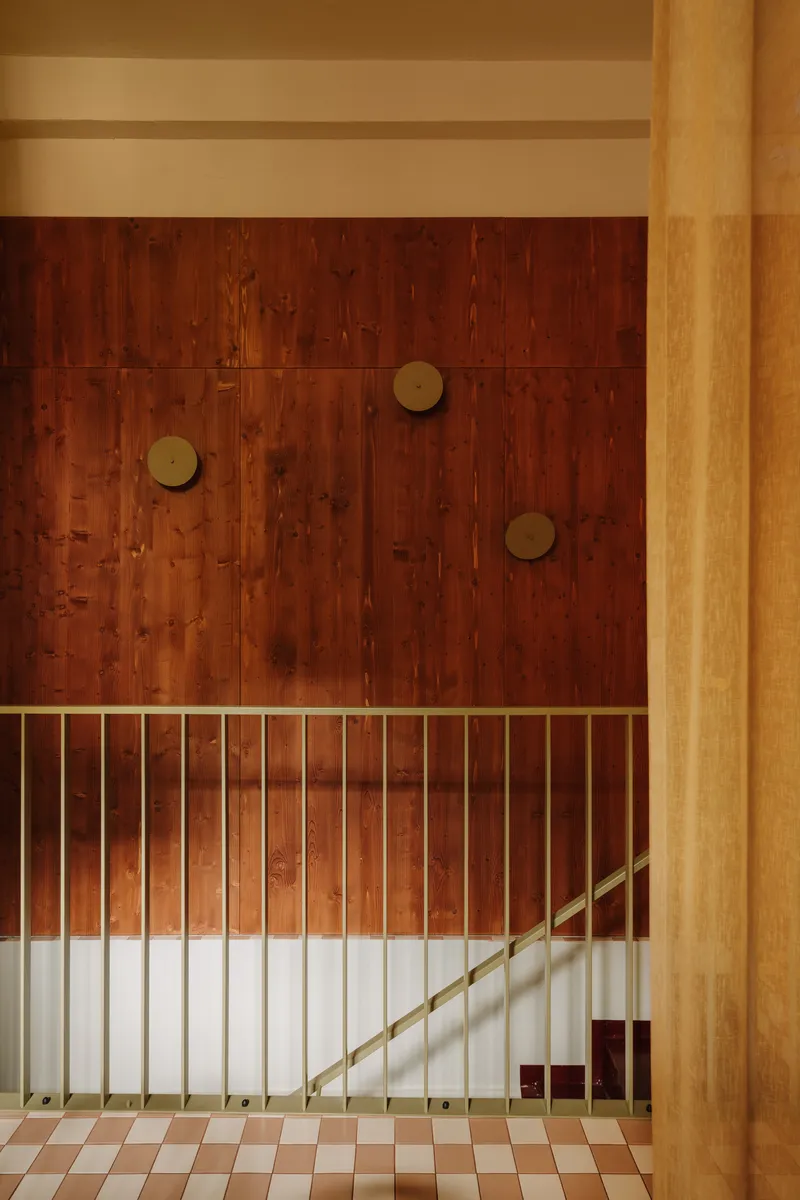 View of the stairwell with vertical brass railings and timber column beside chequered tile floor