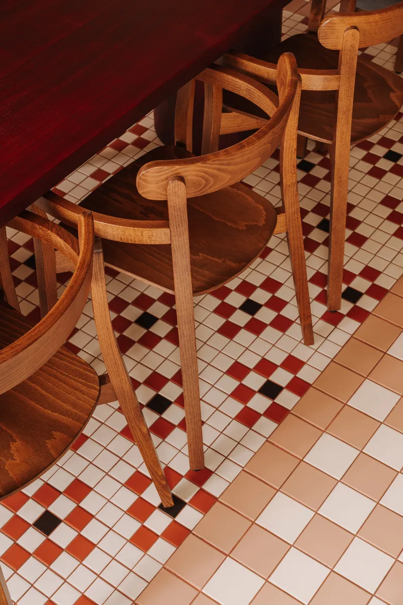 Overhead view of timber chairs arranged on diagonal chequered tile floor in warm light