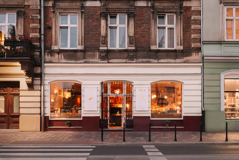 Street facade with arched storefront windows and dark maroon base below white stucco at dusk