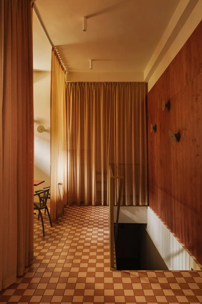 Corridor with floor-to-ceiling curtain divider and checkered tile floor in warm afternoon light