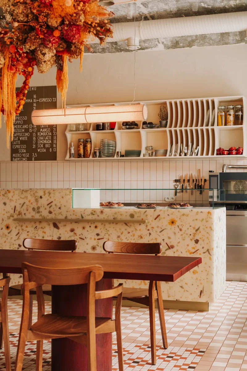 Service counter clad in terrazzo with dried flower installation hanging from the exposed ceiling joists