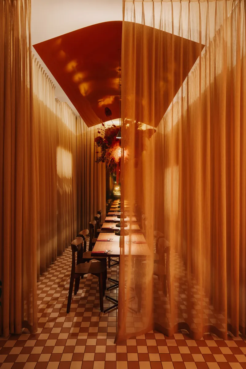 Long corridor with sheer curtains and red ceiling panel leading to suspended floral arrangement