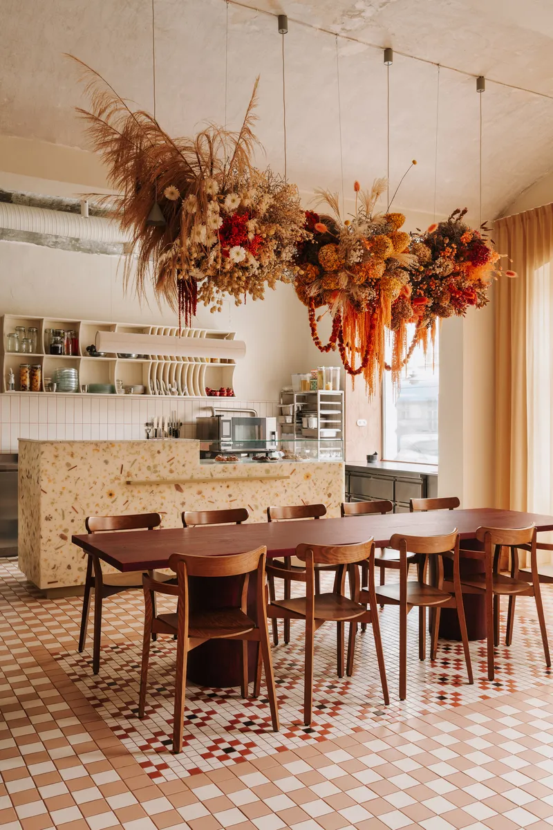 Dining room with large dried floral installation above timber table and chipboard service counter