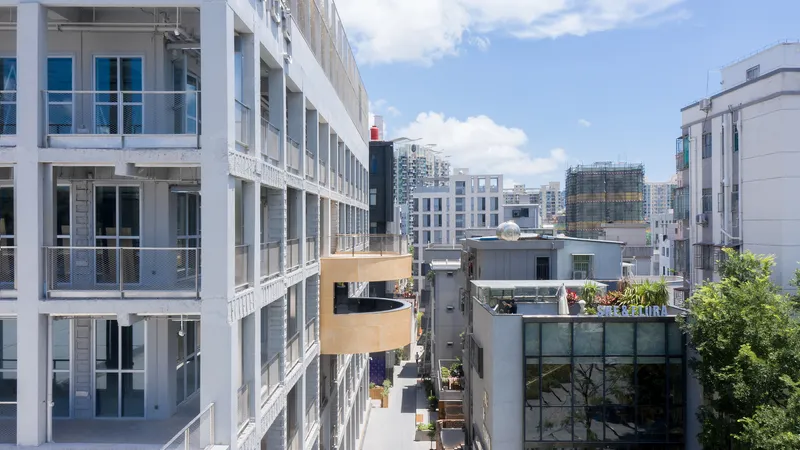 White concrete frame facade with glass infill facing a narrow alley and neighboring rooftops