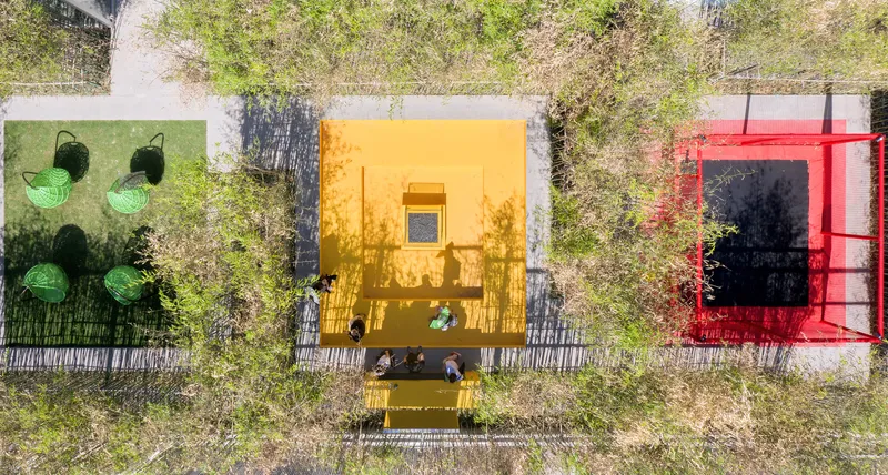 Aerial view of three brightly colored courtyard volumes with seating areas surrounded by bamboo groves