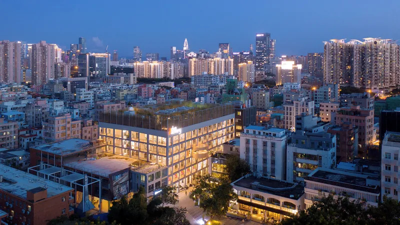 Rooftop view of the glowing facade framed by surrounding urban towers at blue hour