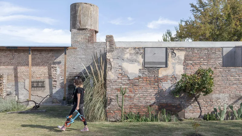 Weathered brick compound wall with concrete water tower and planted bed where a child plays on grass