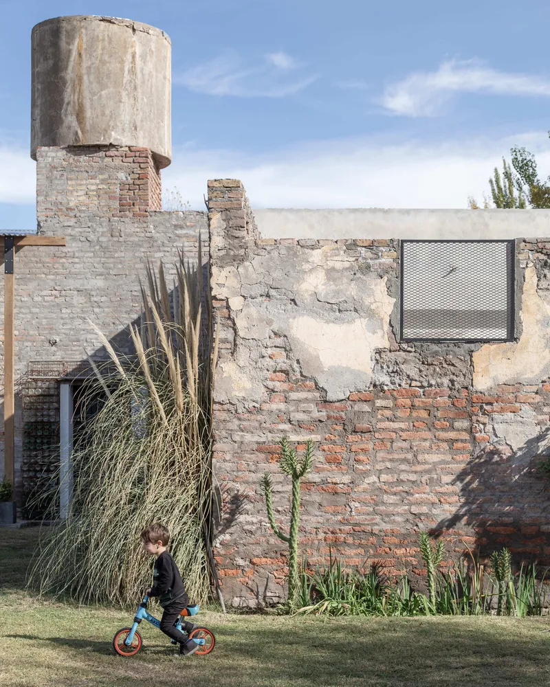 Exposed brick wall with concrete water tower and tall bundled grasses beside a child on a bicycle