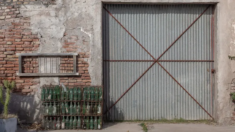 Corrugated metal door with diagonal red bracing set into a patched brick and stucco facade