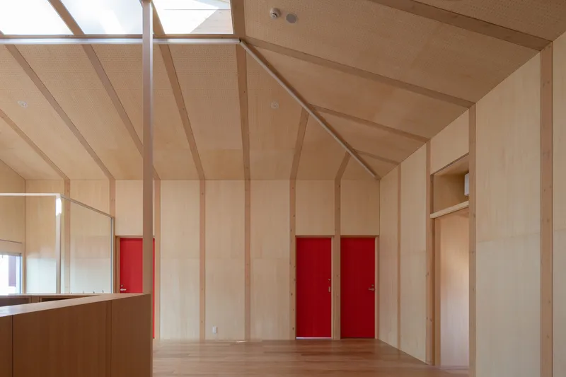 Plywood-lined room with vaulted ceiling, exposed timber ribs, and red sliding doors set into the wall