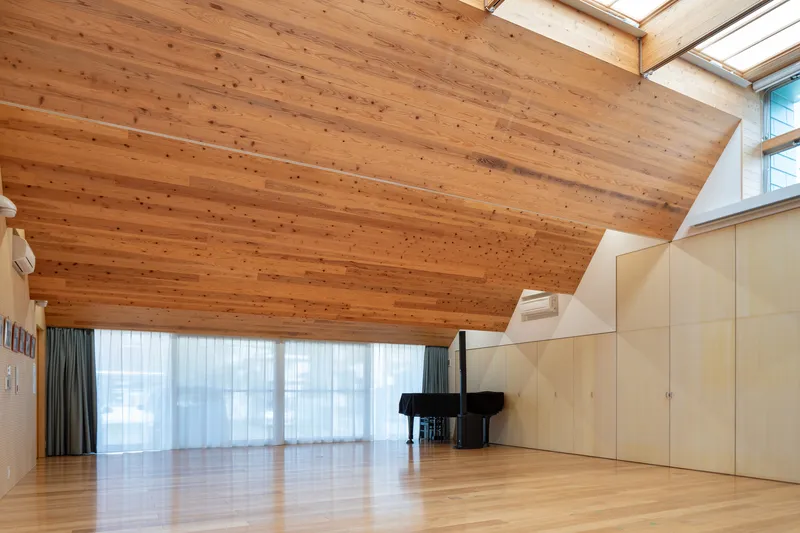 Performance hall with exposed timber ceiling planks, sheer curtains over windows, and a grand piano on the floor