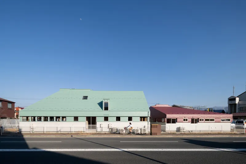 Street view of the building with a pale green pitched roof and continuous ribbon windows along the base