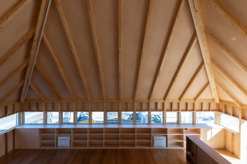 Upper level interior with radiating timber rafters and clerestory windows framing a snowy landscape