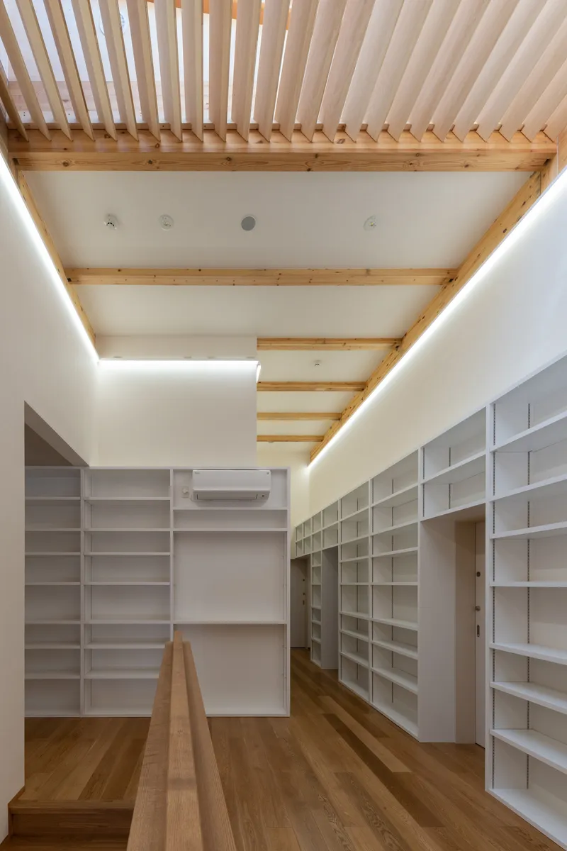 Library room with floor-to-ceiling white shelving and exposed timber beams above indirect cove lighting
