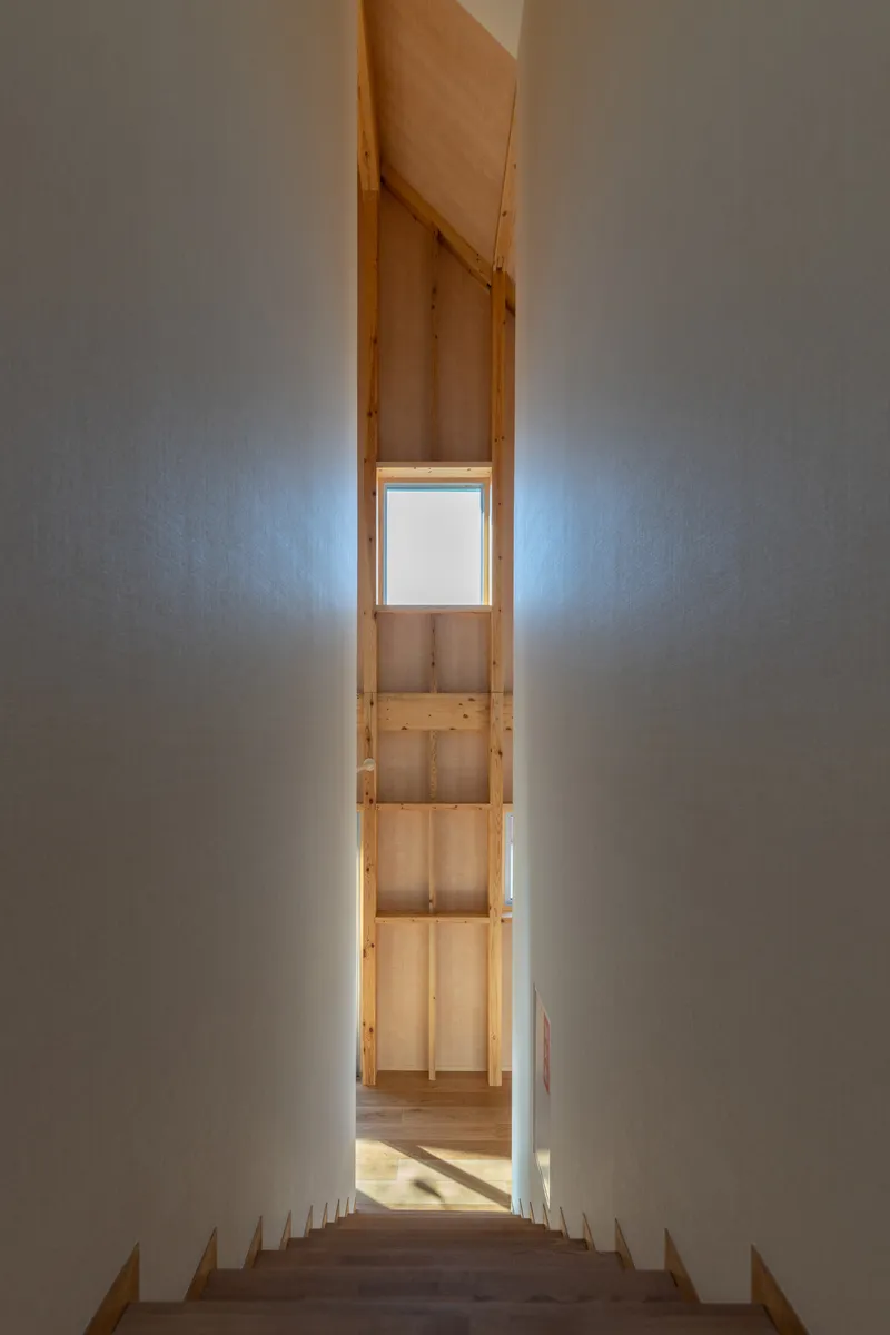 View down a timber staircase toward a narrow landing with a square window framing daylight
