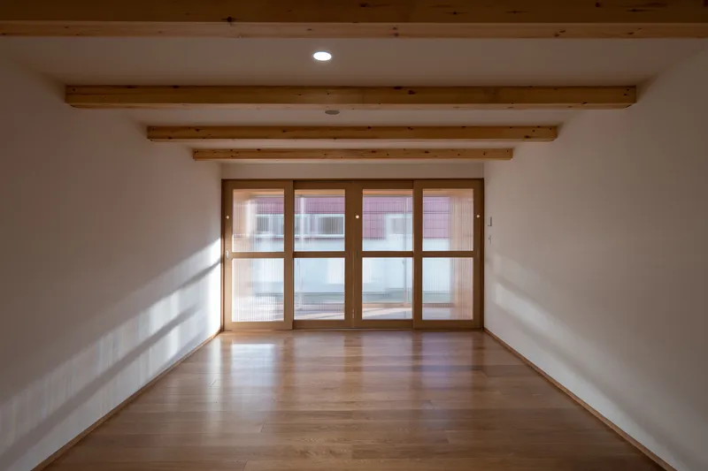 Empty room with timber-framed glazed doors casting geometric shadows across the oak floor