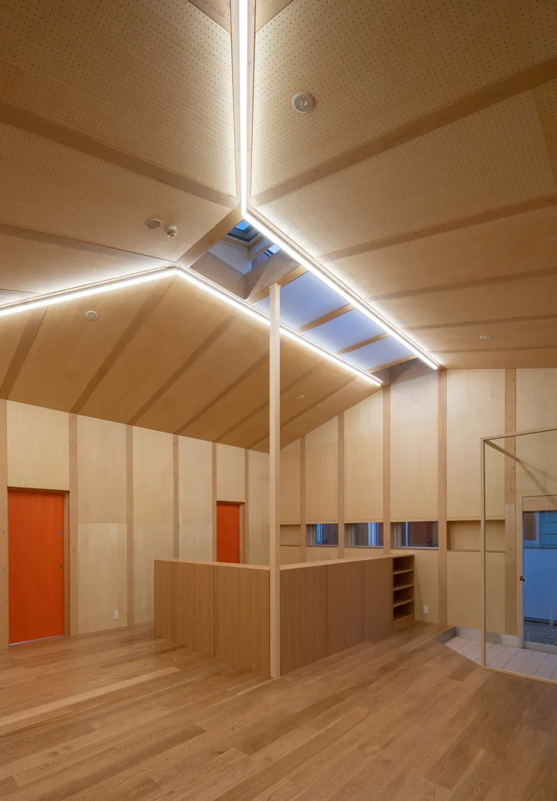 Double-height space with plywood paneling, gabled ceiling, and central island beneath a skylight at dusk