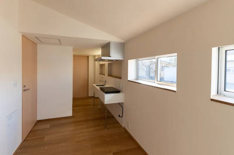 Compact kitchen with stainless steel range hood and horizontal windows overlooking neighboring rooftops
