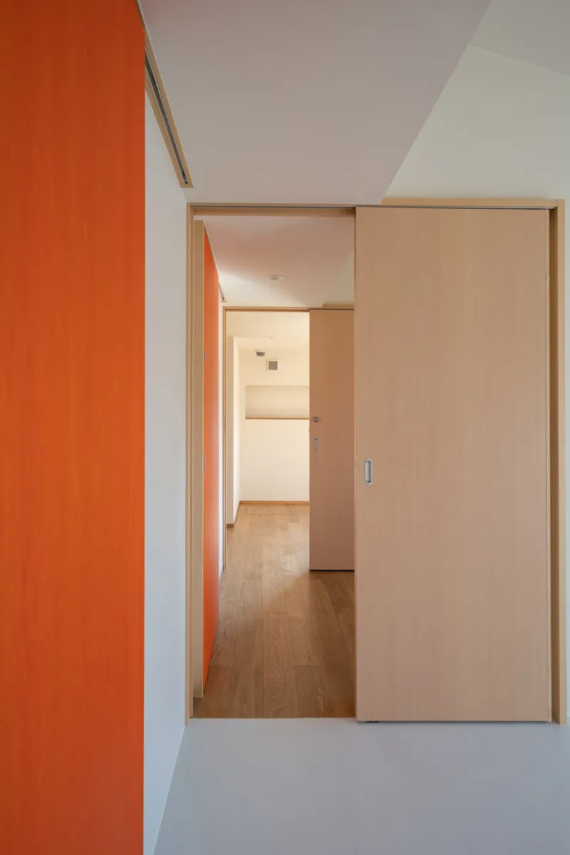Sliding wood door opening onto a corridor framed by an orange accent wall