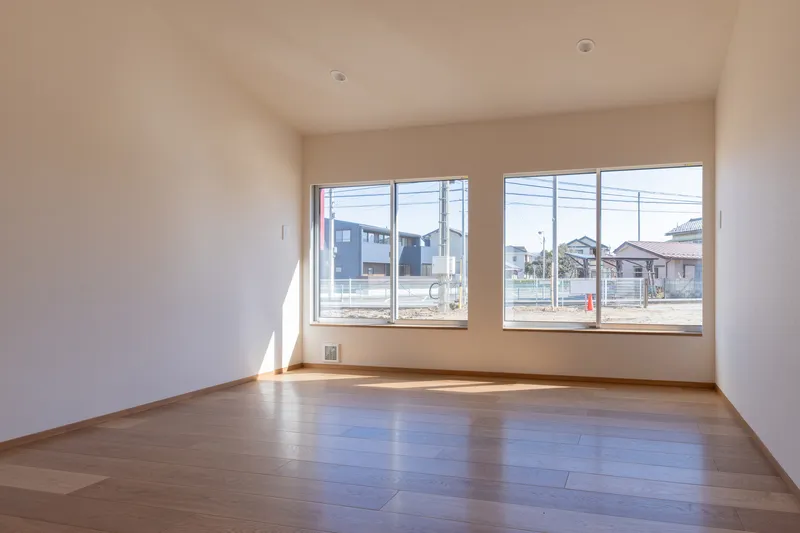 Empty room with pale wood flooring and paired windows casting angular sunlight across the floor