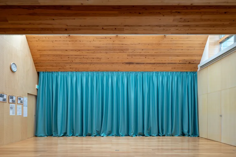 Hall with teal fabric curtain beneath an exposed timber plank ceiling and clerestory glazing