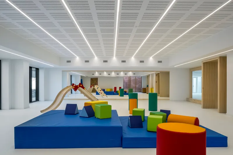 Play area with colorful foam blocks and wooden slide beneath white ceiling with radial light strips